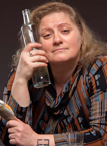 женщина с бутылкой водки смотрит в камеру