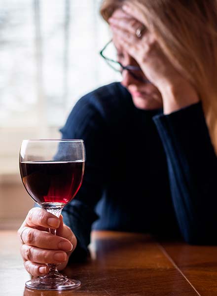 грустная женщина сидит за столом с бокалом вина в руке