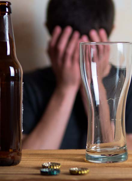 бутылка пива и стеклянный бокал на фоне грустного мужчины