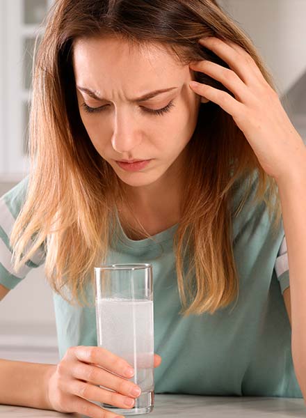 женщина с плохим самочувствием сидит за столом со стаканом воды в руке